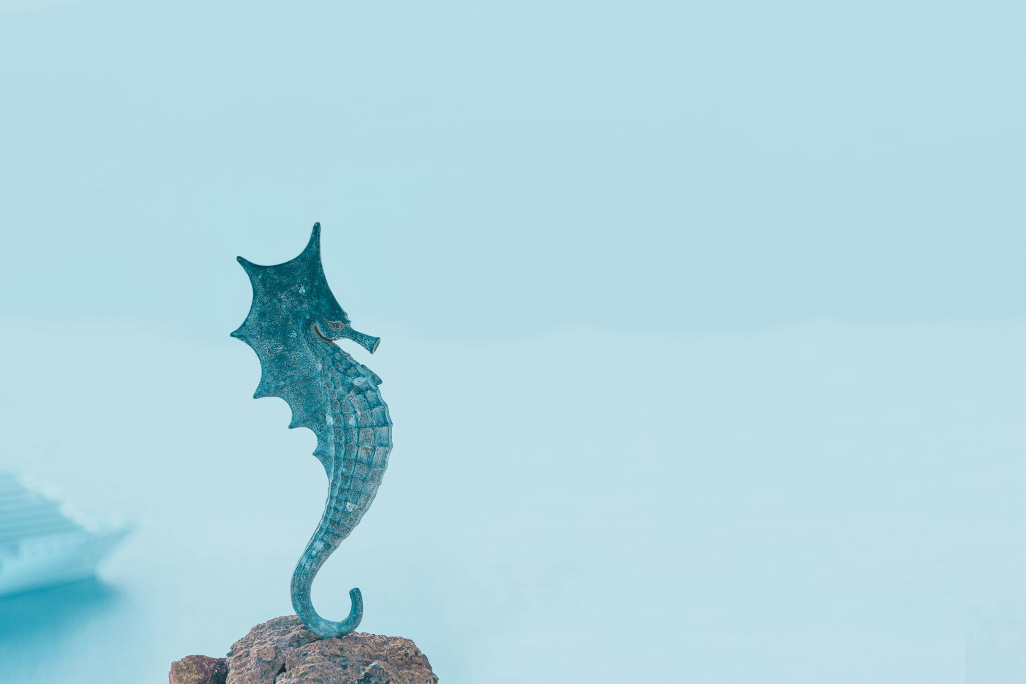 A seahorse sculpture stands on a rock with a cruise ship in the background, Thera, Greece.