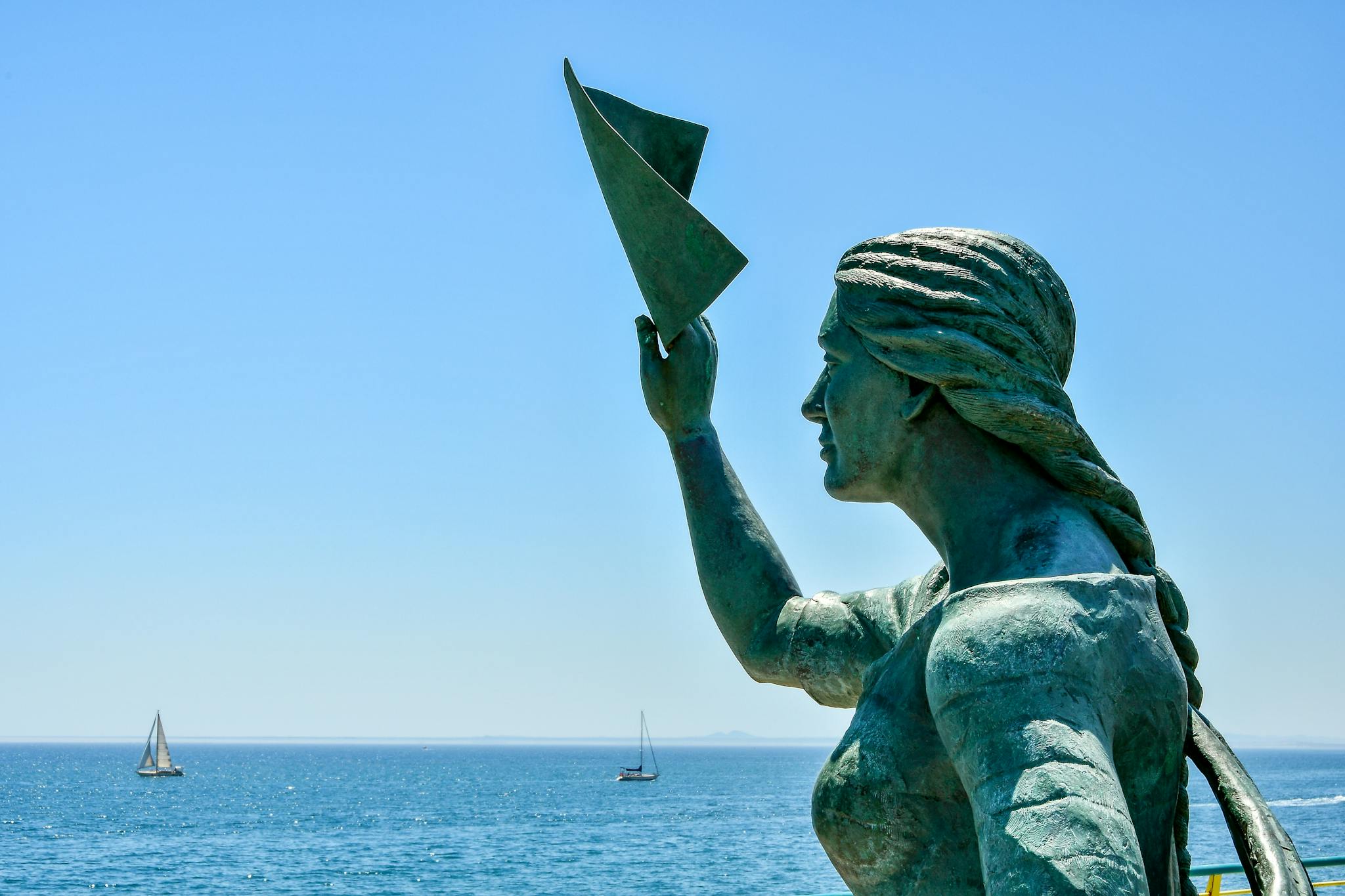 A striking statue facing the horizon with yachts in Torrevieja, Spain under a clear blue sky.